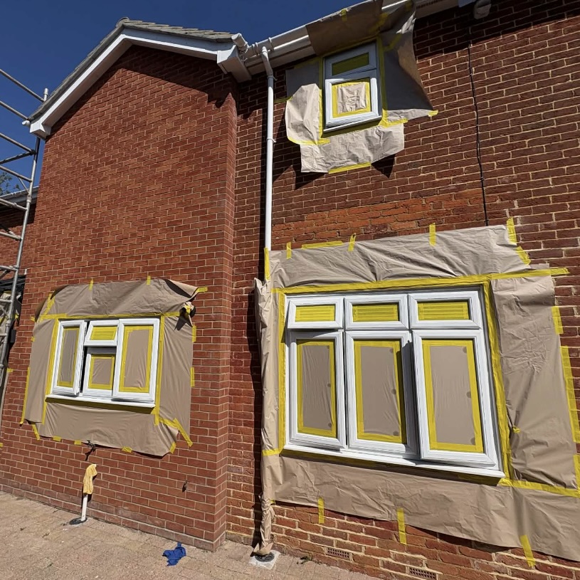 Red brick house with windows fully masked in preparation for UPVC spraying