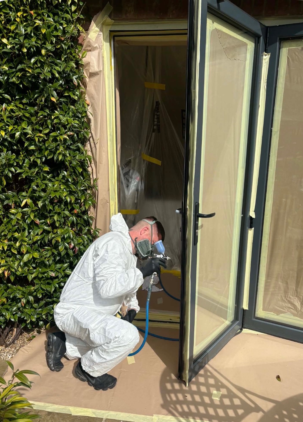 Newlook operator in full PPE spraying a UPVC front door on-site