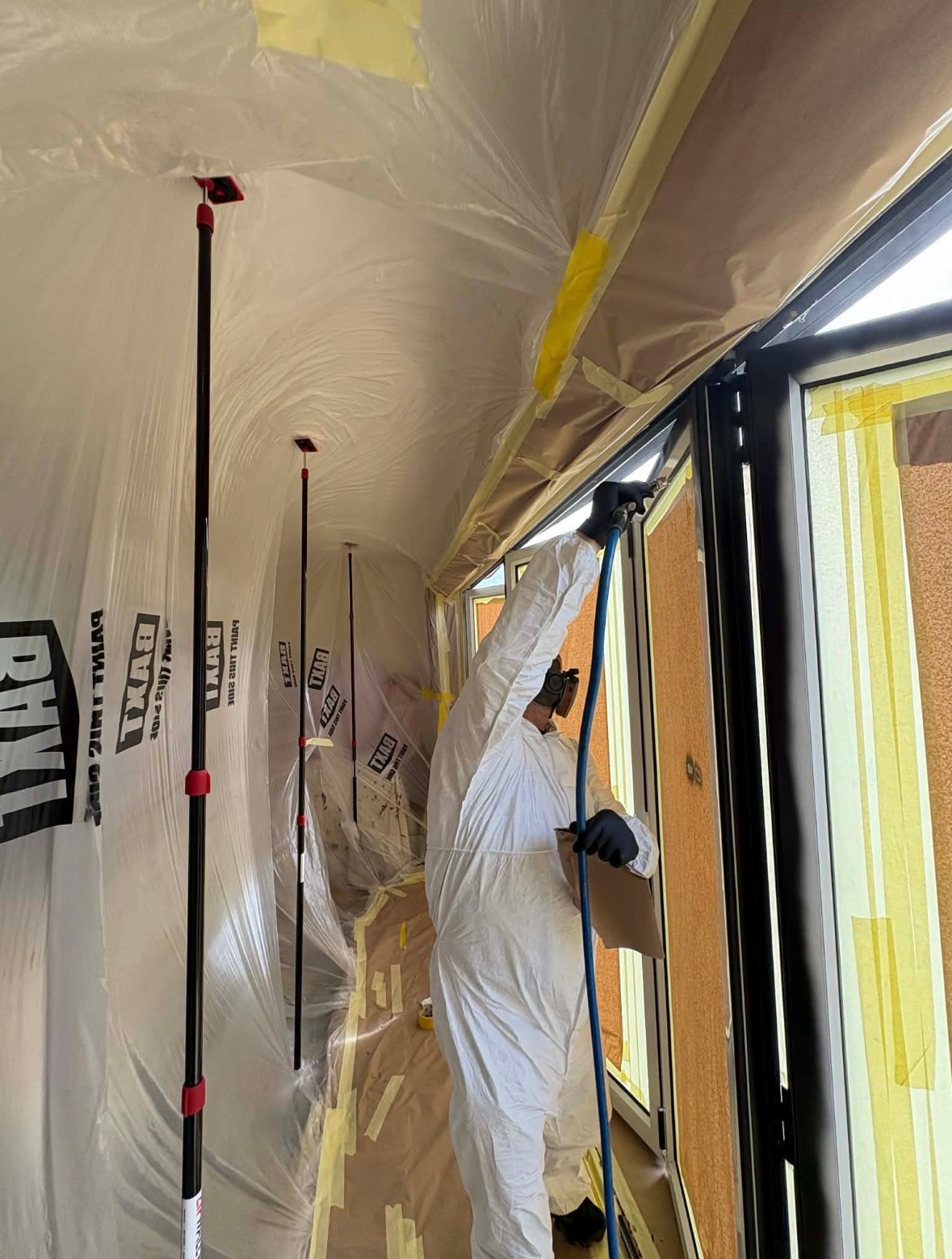 Newlook operator spraying inside a fully masked room with containment sheeting